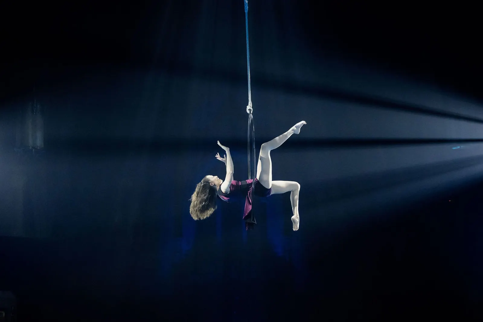 Artiste aérienne suspendue à un tissu sous des faisceaux de projecteurs